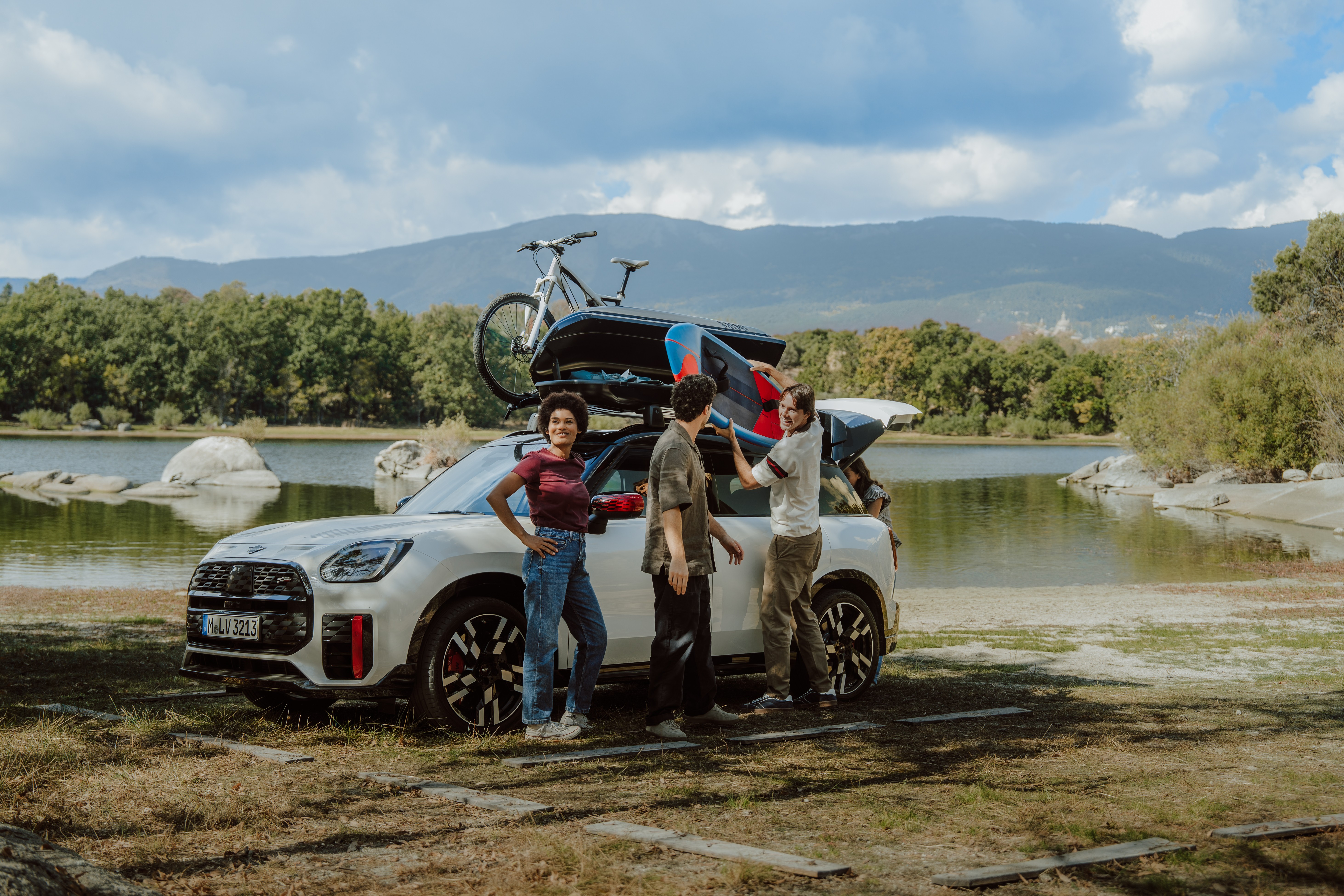 Pessoas ao lado de um MINI equipado com acessórios de viagem originais estacionado na natureza